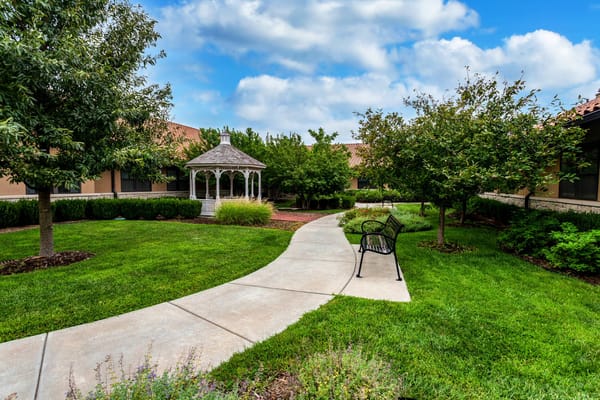 A white gazebo surrounded by lush green grass and trees.