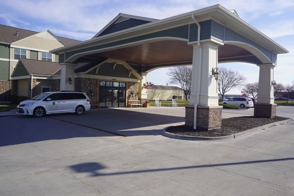Covered entrance with seating and parked vehicles at Remington Heights Retirement