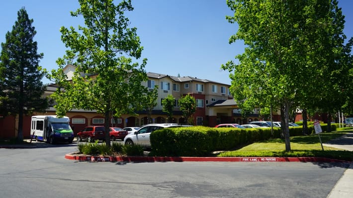 Exterior view of assisted living facility with trees and vehicles