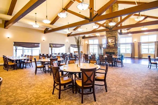 A spacious dining room with tables and chairs, featuring wooden beams and large windows.
