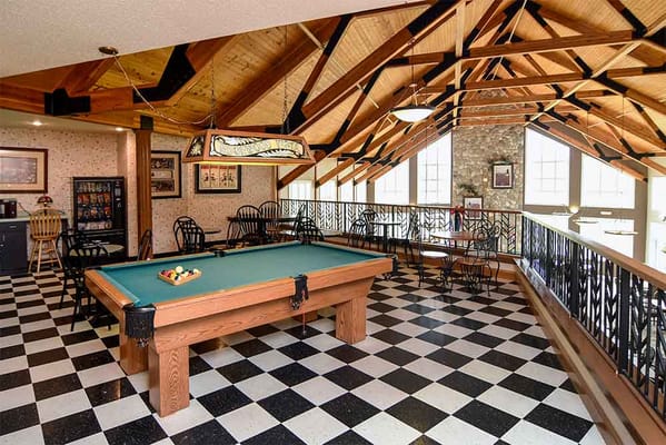 A pool table in a game room with black and white checkered flooring and wooden beams.