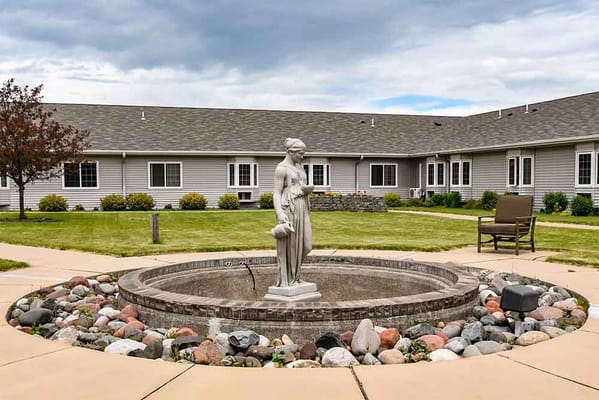 A statue in a courtyard surrounded by landscaped greenery and stone path.