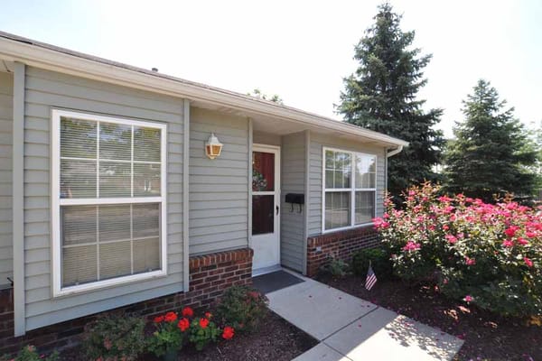 Entrance of a senior living facility with flowers and a porch.