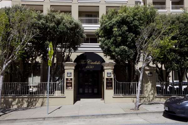 Front entrance of The Carlisle senior living facility with trees lining the walkway.