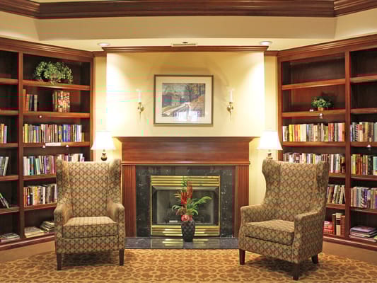 Two patterned armchairs in a library with shelves of books and a fireplace