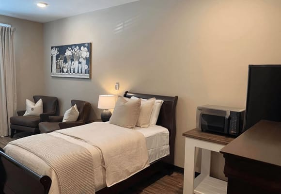 A well-decorated bedroom featuring a bed, two armchairs, a lamp, and a microwave.