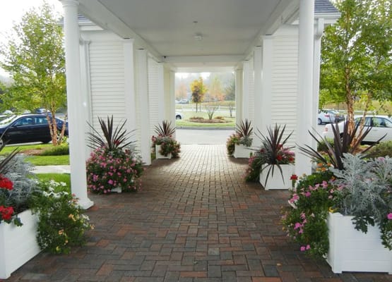 Brick pathway lined with colorful flower planters at the entrance of Maples Senior Living.