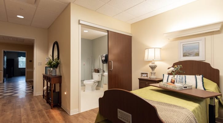 A view of a cozy bedroom in Ridgecrest Rehab, featuring a bed, lamp, and a small table.