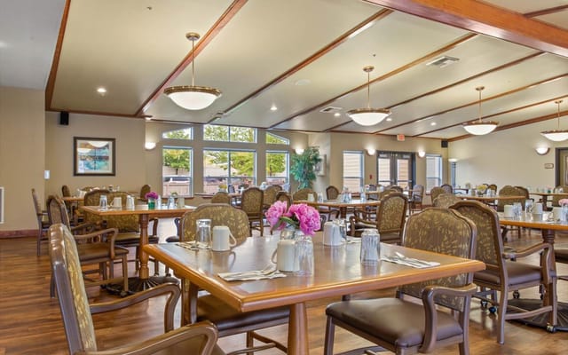 Spacious dining room with tables set for meals and flowers as centerpieces.