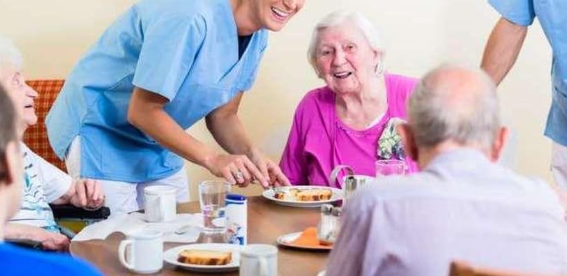 Residents enjoying a meal with attentive staff in a dining area