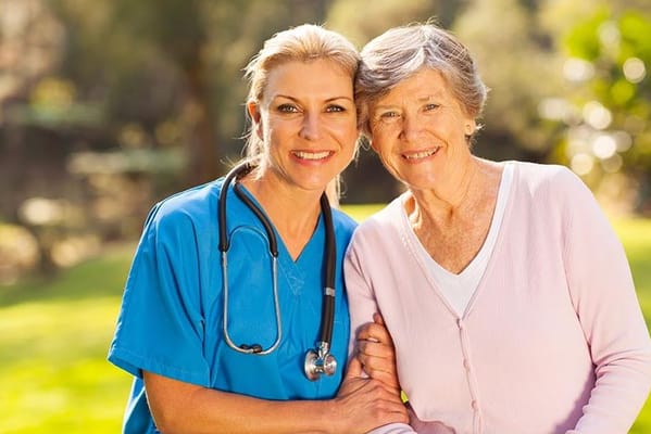 A nurse and a resident smiling together outdoors.