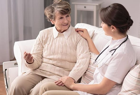 A senior resident and a caregiver sharing a warm conversation on a couch.
