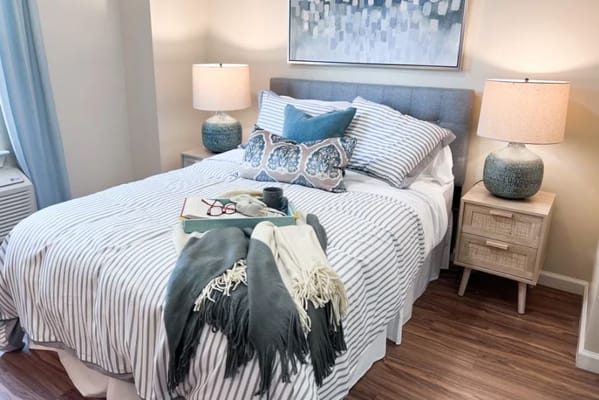 A well-decorated bedroom featuring a striped bedspread, cozy pillows, and bedside lamps.