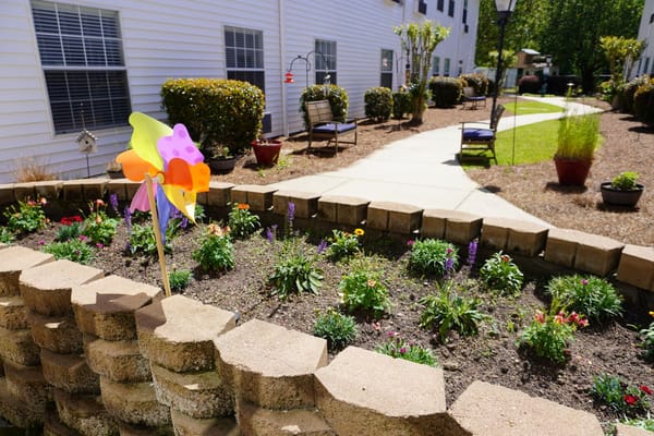 A vibrant garden with flowers and a colorful pinwheel in front of a building.
