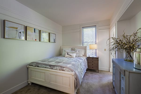 A well-decorated bedroom with a bed, lamp, and artwork on the wall.
