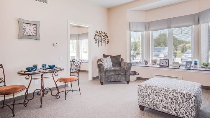 A cozy living room with a table set for tea, a comfortable chair, and a decorative ottoman.