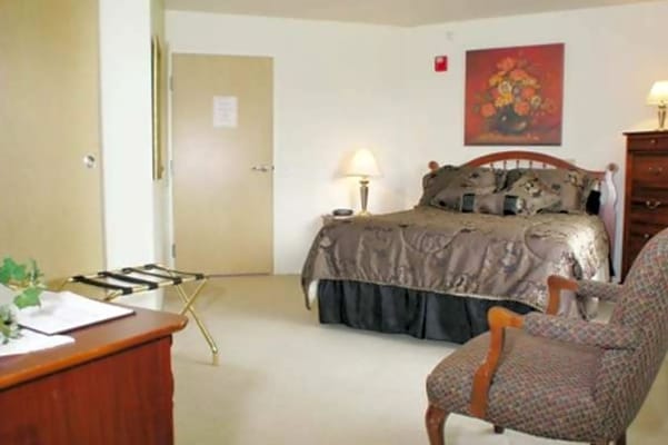 A cozy bedroom featuring a bed, chair, and desk in Sunbury Village.