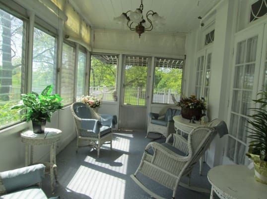 A sunroom with wicker chairs and plants, filled with natural light.
