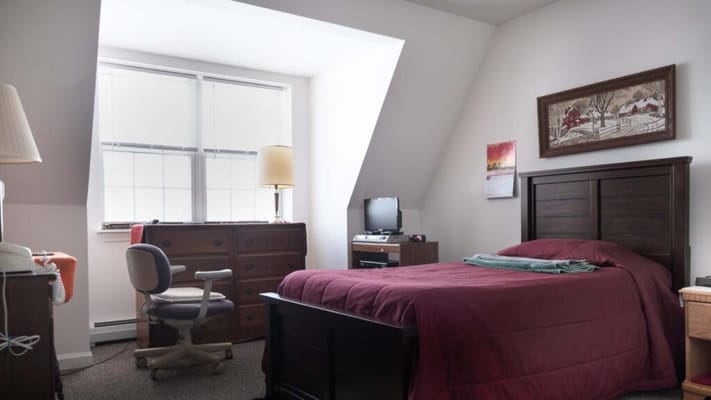 A bedroom with a burgundy bedspread, desk, and large windows.
