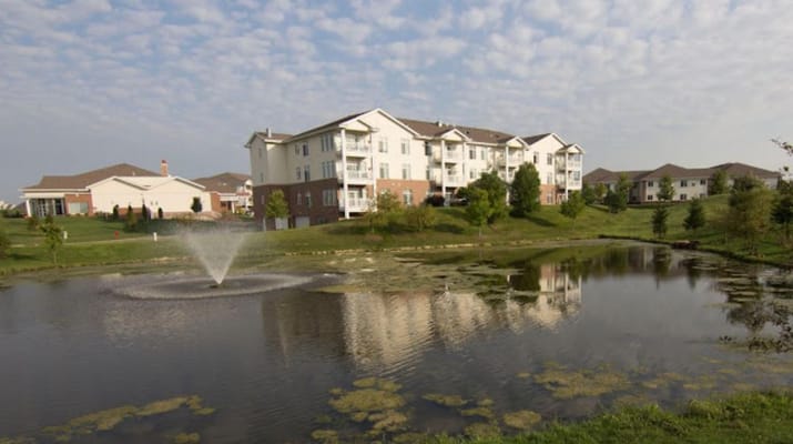 View of a pond with a fountain and residential buildings in the background