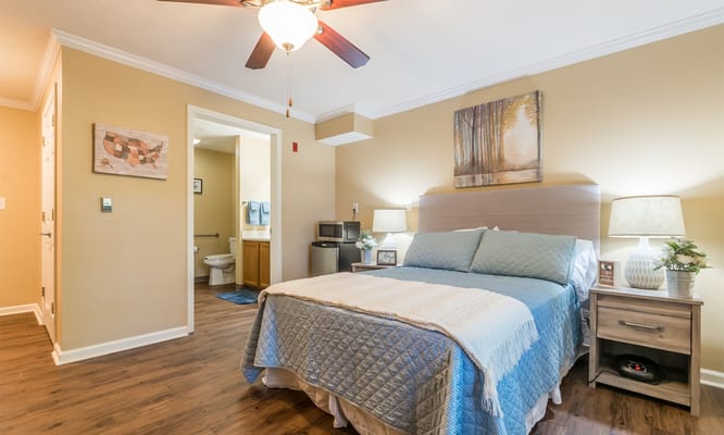 A cozy bedroom featuring a bed with a blue quilt, lamps, and artwork.