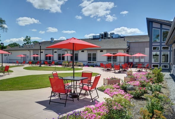 Outdoor seating area with red umbrellas and vibrant flower beds.