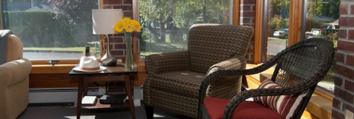 A comfortable sitting area with a cozy chair, table, lamp, and flowers.