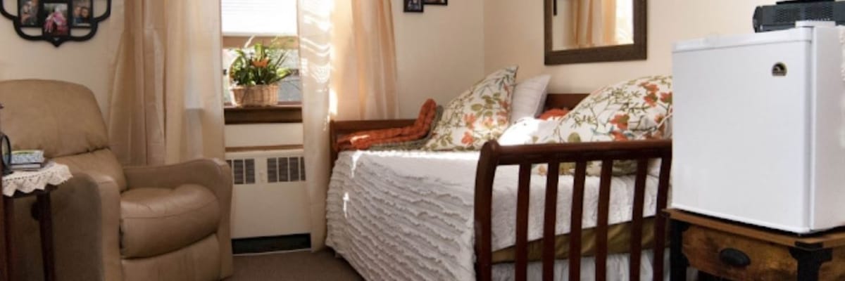 A cozy bedroom featuring a bed, chair, and mini fridge