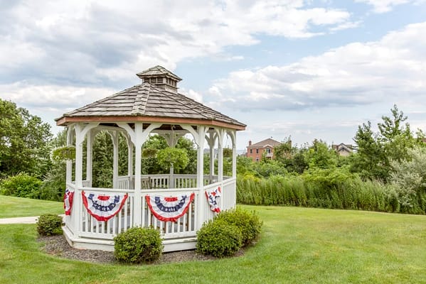 White gazebo decorated with red, white, and blue bunting in a green yard