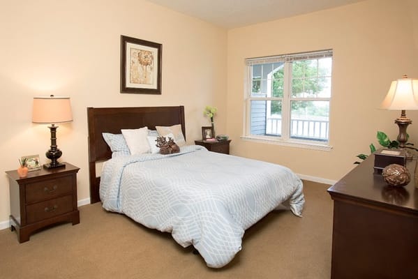 A well-lit bedroom featuring a bed, nightstands, and a window.