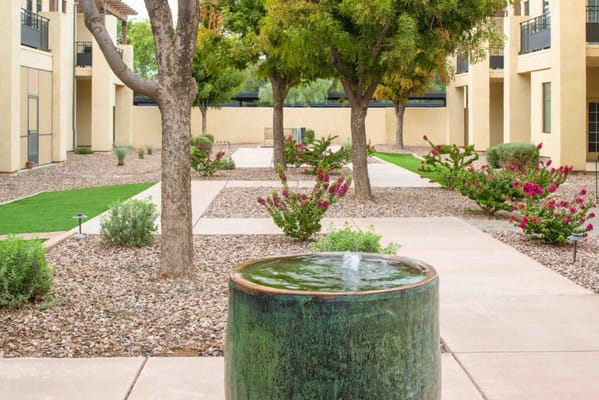 A serene garden with a fountain surrounded by trees and flowers.