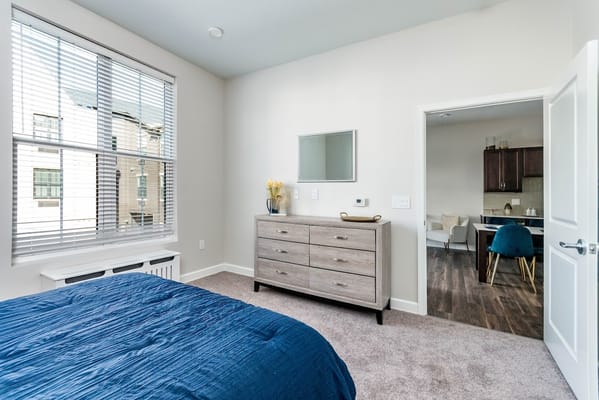 A cozy bedroom with a blue bedspread, dresser, and access to a living area.