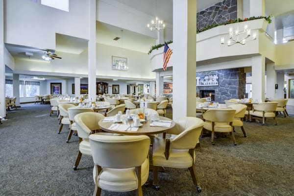 Bright dining area with round tables and chairs in a senior living facility.