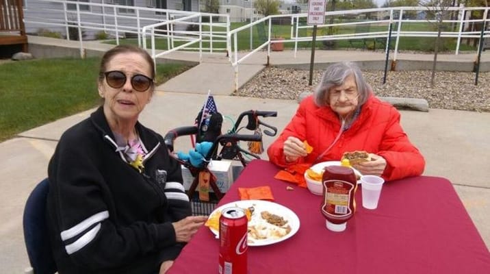Two senior women enjoying lunch at a table outdoors