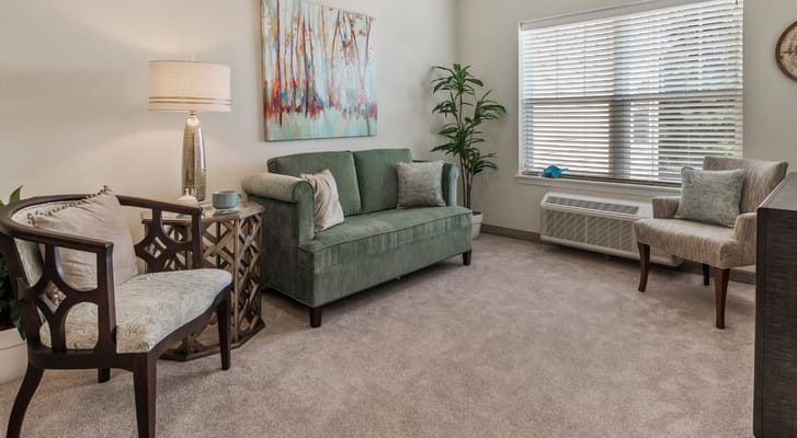 Cozy living room featuring a green sofa, wooden chairs, and decorative art.