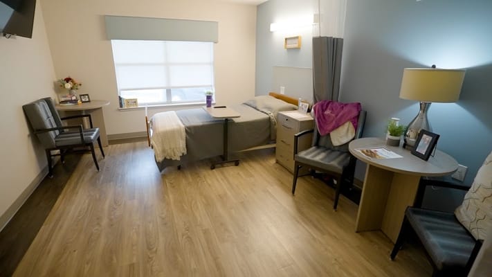 A well-furnished bedroom in a senior living facility with a bed, chairs, and decorative items.