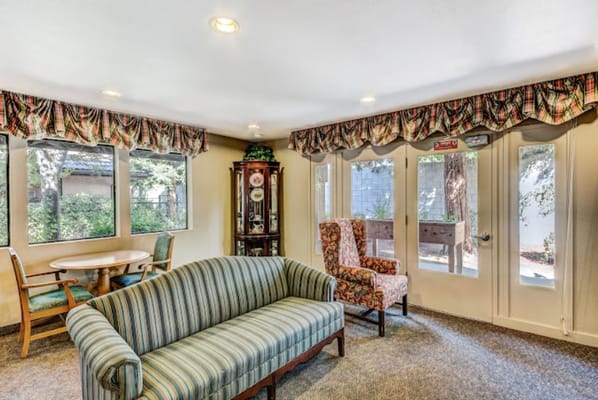 Cozy living room with a striped couch, floral chair, and dining table near large windows.
