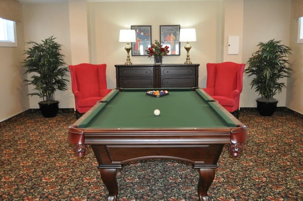 Billiards table in a cozy lounge area with red chairs.
