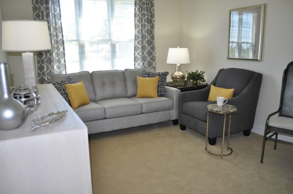 A stylish living room featuring a gray couch with yellow pillows, a gray armchair, and a side table.