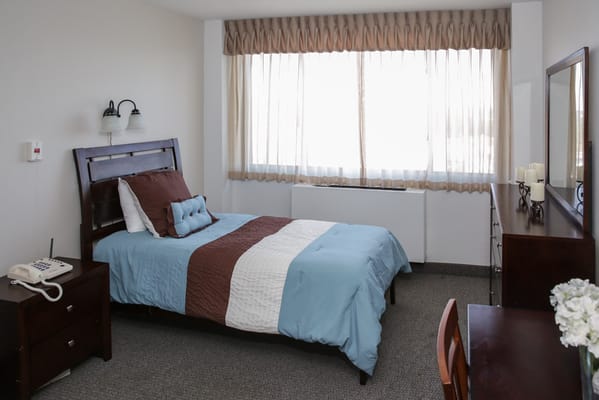 A neatly arranged private resident room with a bed and window