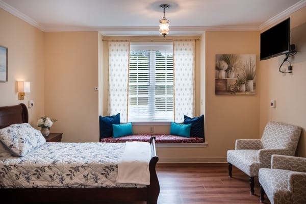A cozy bedroom with a bed, seating area, and large window.