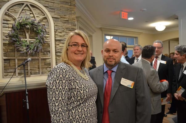Two people posing at a facility event with attendees in the background