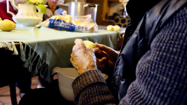 Senior peeling potatoes at a dining table