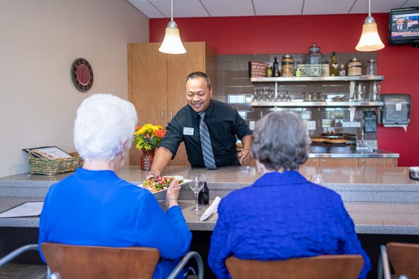 Staff member serving food to residents in dining area