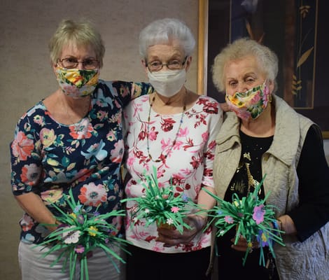 Three residents holding craft flowers indoors
