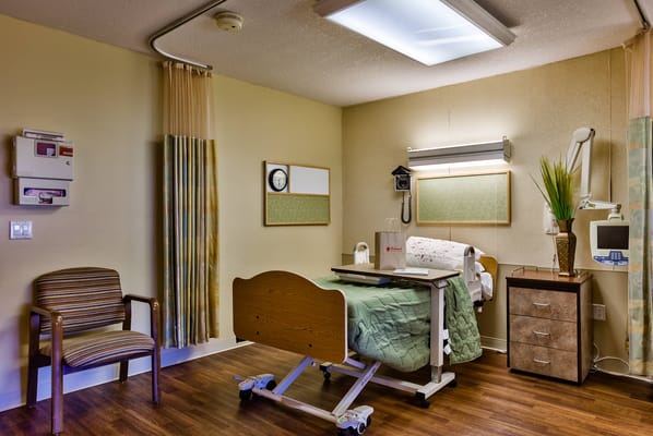 A private room in a senior living facility with a bed and chair