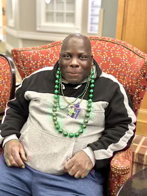 Resident sitting in a colorful armchair with festive beads