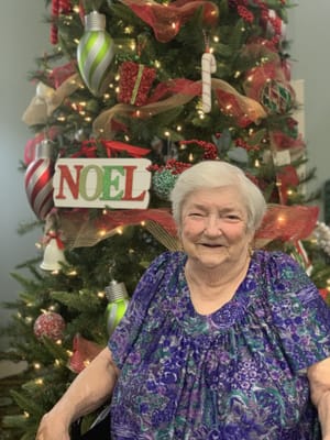 Resident smiling in front of a decorated Christmas tree