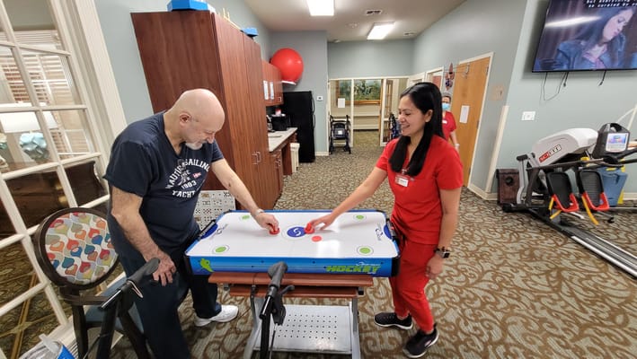 Resident and staff member playing air hockey in an activity room