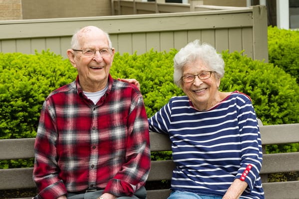 Two seniors smiling on a bench in a garden